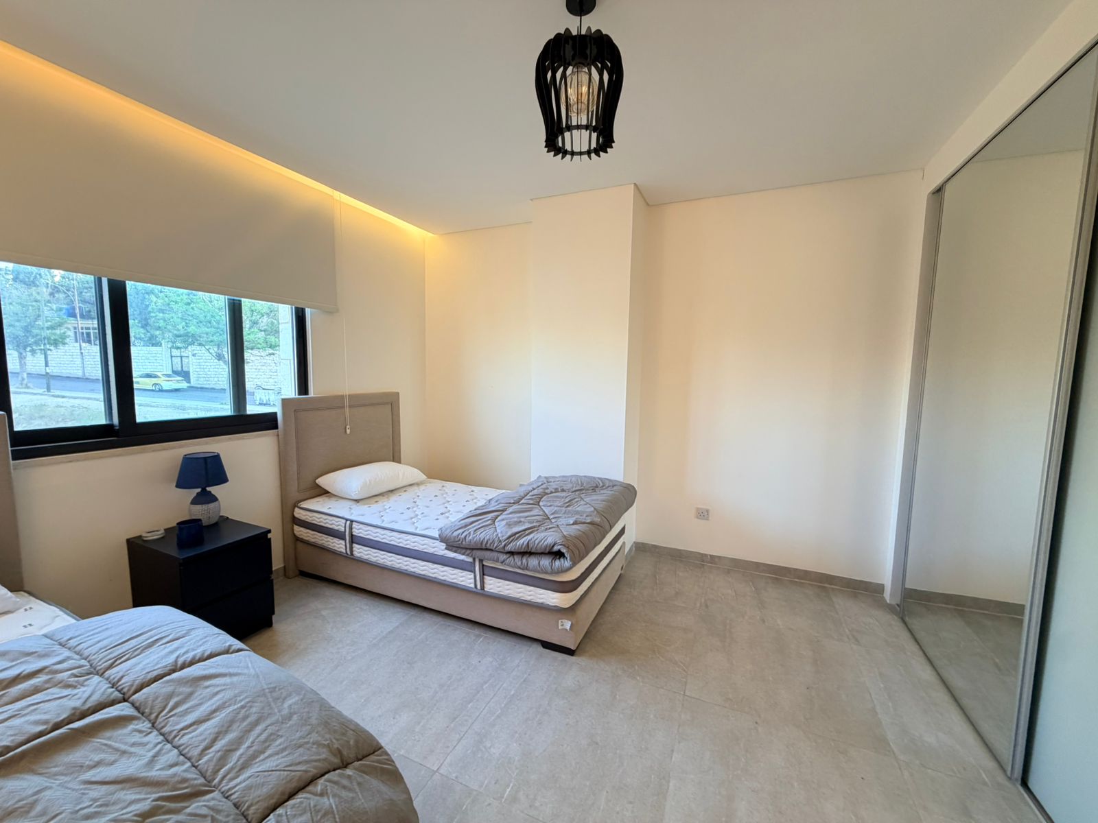 978f4b41-1170-421e-9552-9ad76a766373 Bedroom with two single beds, blue lamp on a black nightstand, and a large mirrored wardrobe along the right wall.