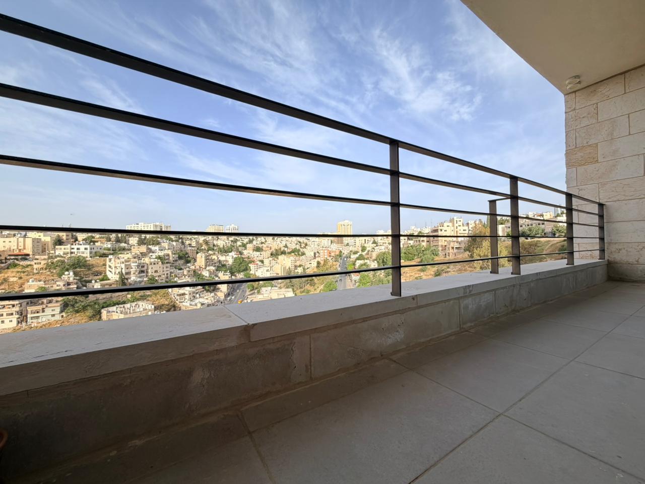 a0528337-3b28-42e3-8464-62a12b097412 Balcony railing with a cityscape and clear blue sky in the distance.