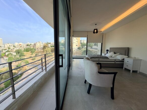 Hotel room with a king bed, two white nightstands, and a balcony overlooking a cityscape.