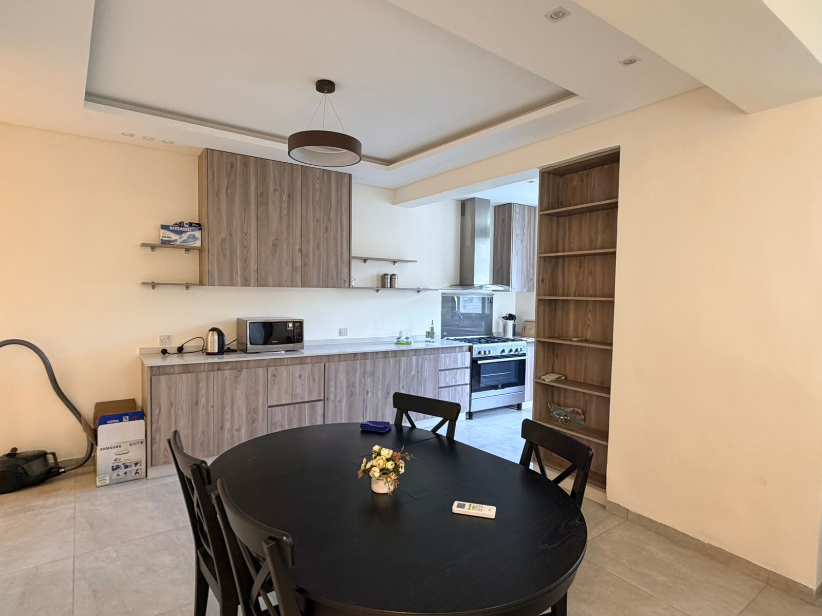 c7d30786-af06-44ba-893d-22cf65784c37 Open-plan kitchen with wood grain cabinets, a round black dining table, and a small flower centerpiece.