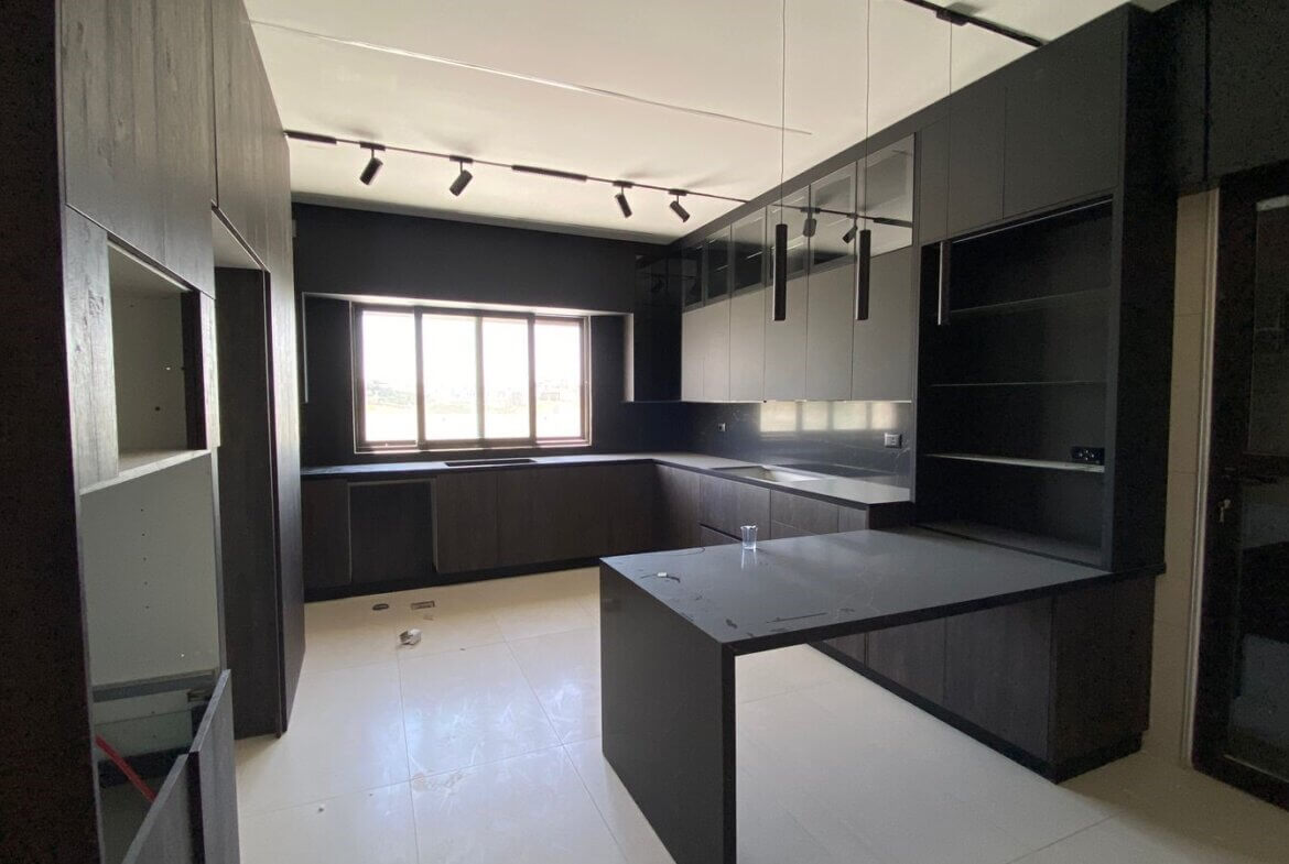 afa1e2d7-c2ef-43ce-bceb-72677e0efc10 Dark minimalist kitchen with black cabinets, an island, and a large window for natural light.