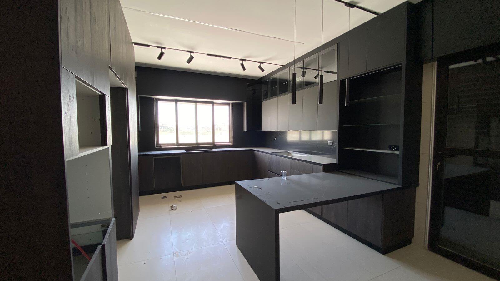afa1e2d7-c2ef-43ce-bceb-72677e0efc10 Dark minimalist kitchen with black cabinets, an island, and a large window for natural light.