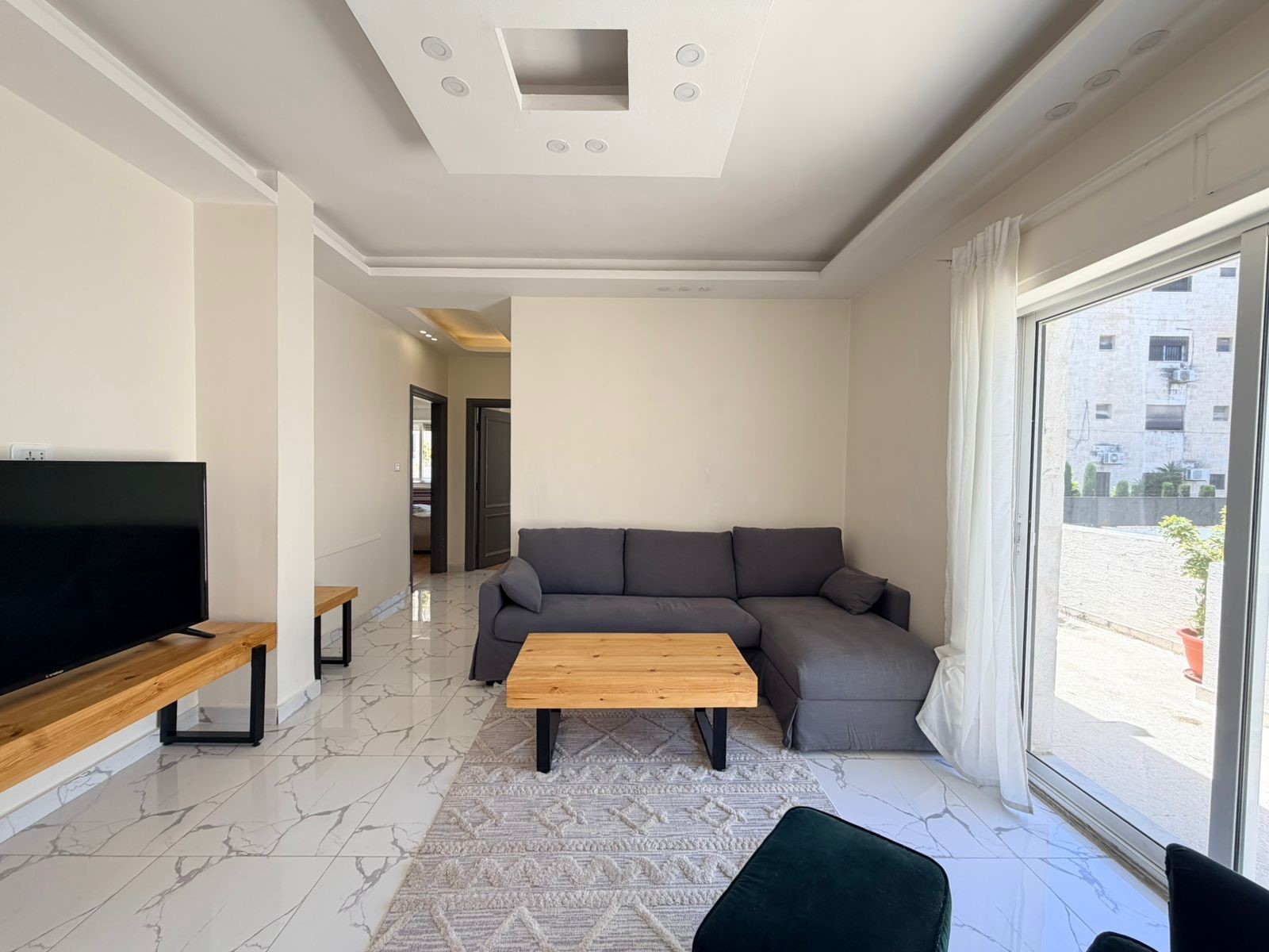 0772f16d-8d42-4227-8a63-1c38d82ee4e5 Bright living room with a gray sectional sofa, wooden coffee table, and a flat-screen TV on a wooden console.