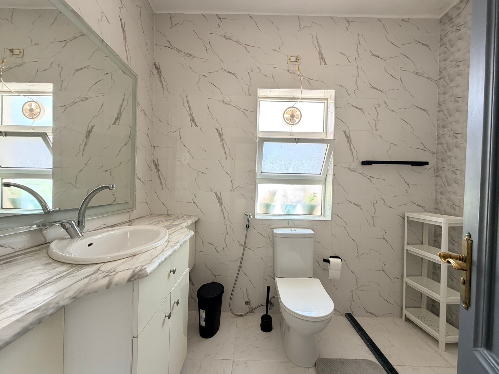 1fc761bf-05c4-4da7-8921-7722910a3644 White marble-tiled bathroom with a marble countertop sink and chrome faucet, large wall mirror, and windowed toilet area.