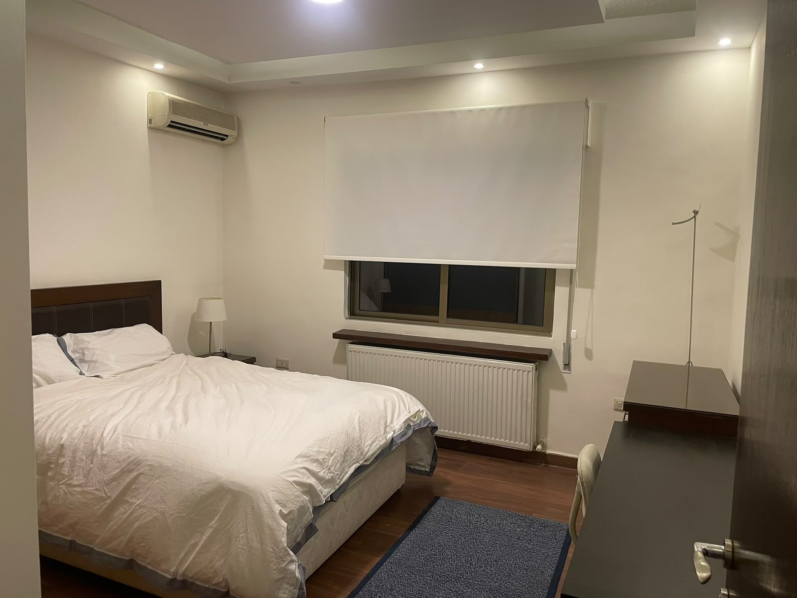 9f771238-64aa-4a20-b591-e3b09ded5344 A modern bedroom with a large bed, white bedding, and a wooden headboard beside a small night lamp.