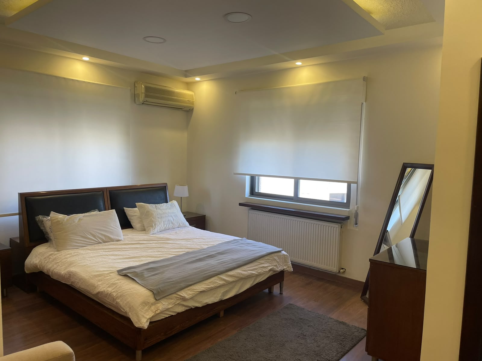 aaa13d9e-832d-4107-a134-91ea7c8f0725 Hotel bedroom with a large wooden bed, white bedding, and two dark headboards against pale walls