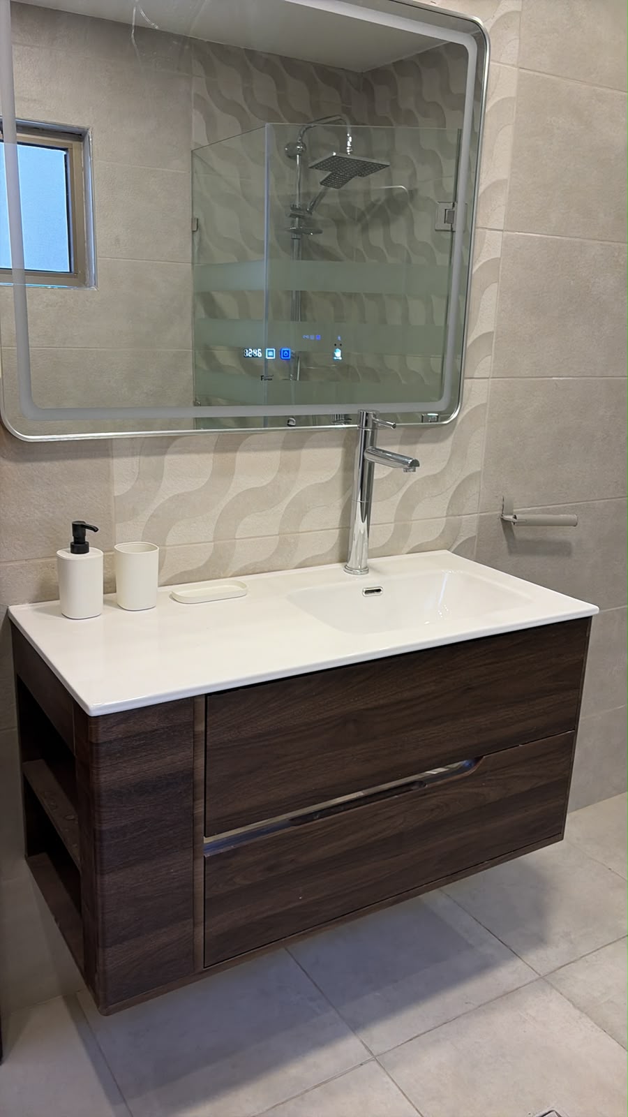 dde56eef-8478-4dce-a092-f981ae1fcc49 Modern bathroom vanity with white countertop, dark wood cabinet, tall chrome faucet, and a frosted-stripe mirror; soap dispenser and cup on the counter.