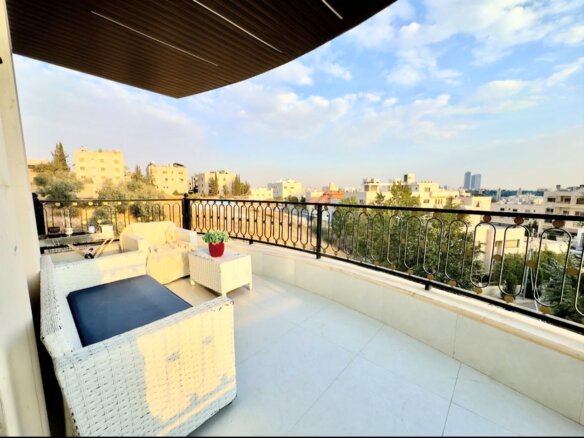 Urban balcony with white wicker seating, navy cushions, and a small potted plant, overlooking a cityscape.