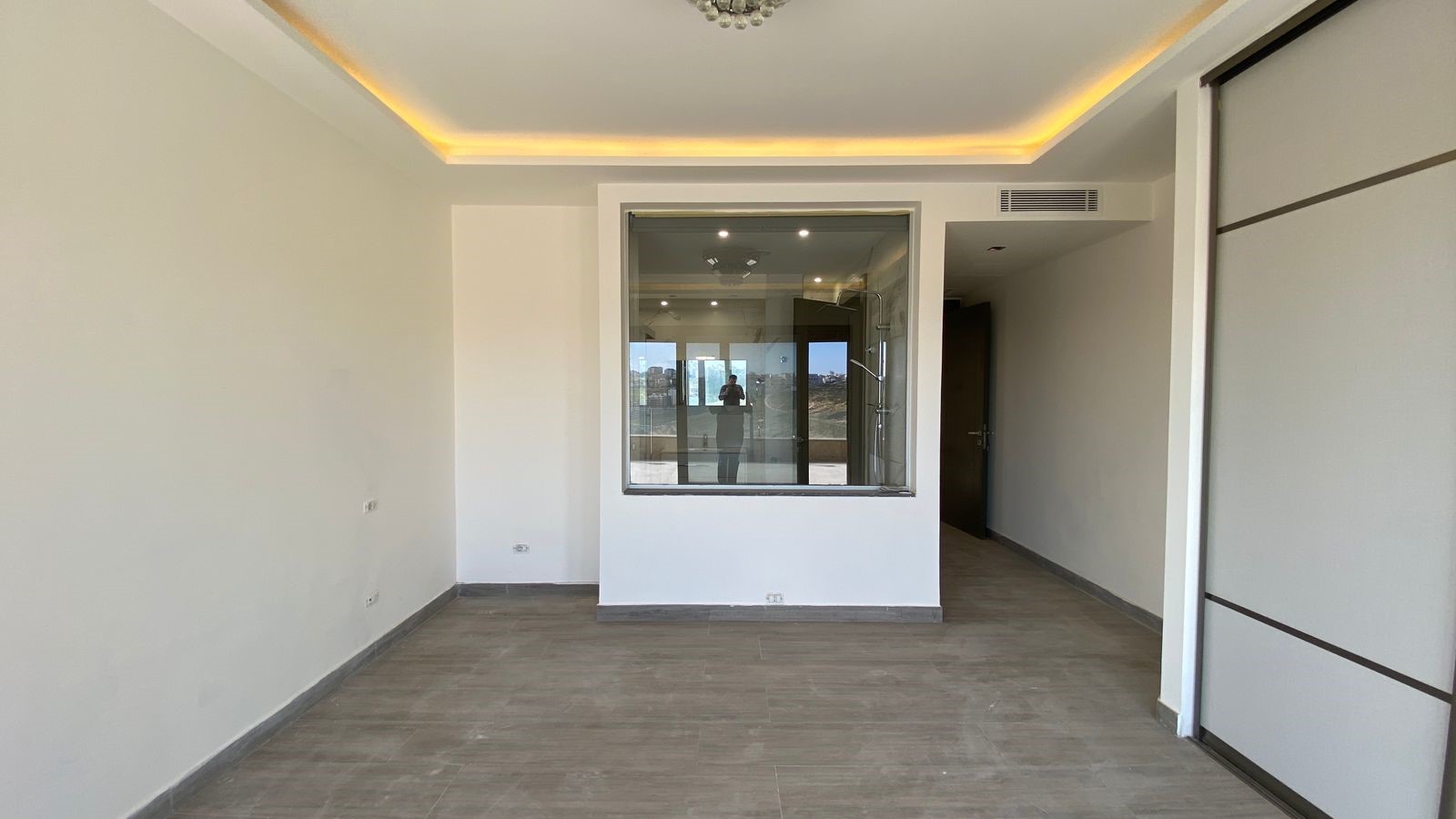 068a5d75-1499-41ab-b6b5-5f0ae0f1521b Empty modern room with gray tile flooring, white walls, and a glass-walled interior space in the center.