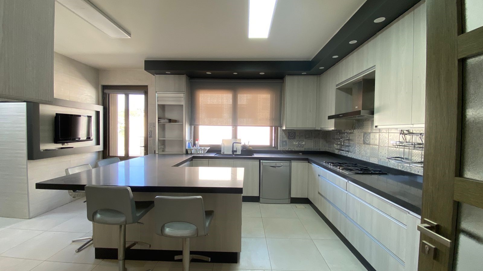 1730d00b-06a1-464a-a1dd-b0b74196ea51 Modern kitchen with central island, gray cabinets, black countertops, and a stovetop along the right wall.