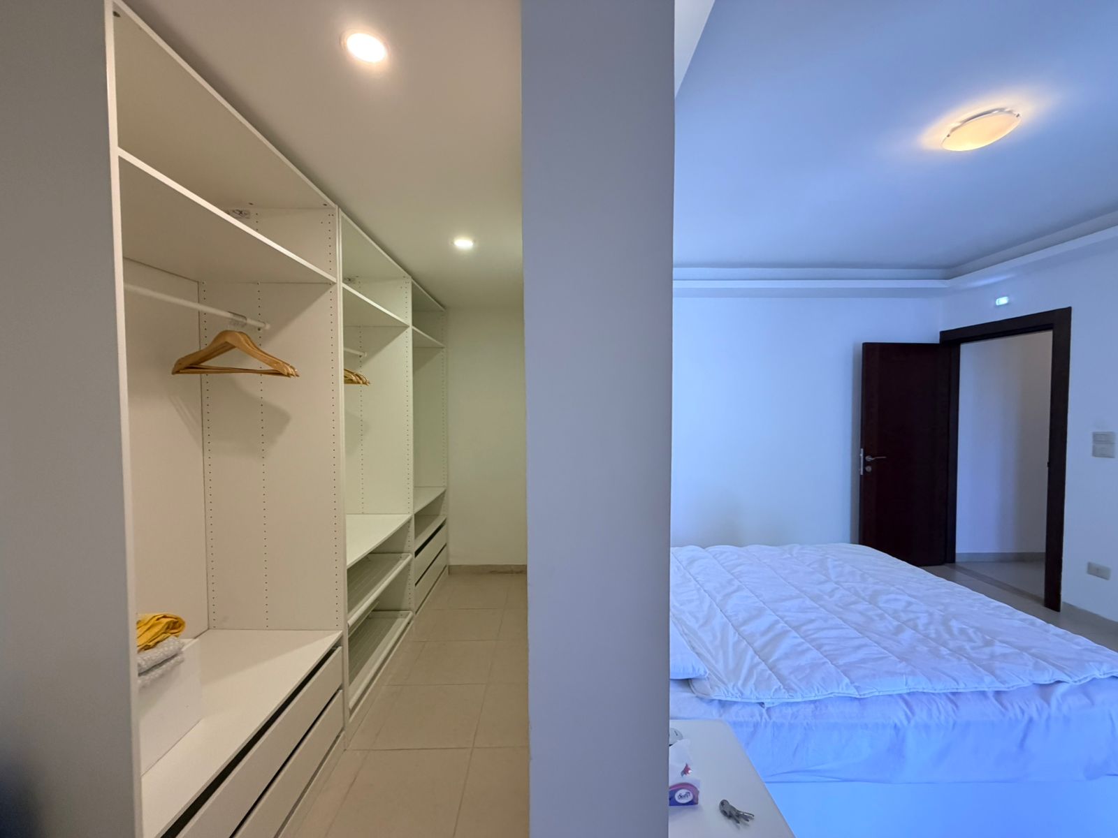 27f61a90-44e7-40d0-8f87-9f2ca35dd926 Modern bedroom with a white open closet system along the left wall, and a neatly made bed on the right side of the room.
