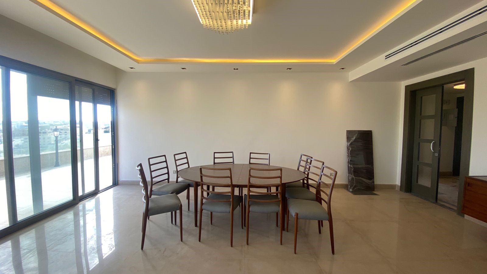 5cd5bda0-7f1f-4361-89d5-693292ec8fc9 Bright meeting room with a large glass sliding door balcony to the left, a round wooden table and ten matching chairs, and a modern chandelier overhead.