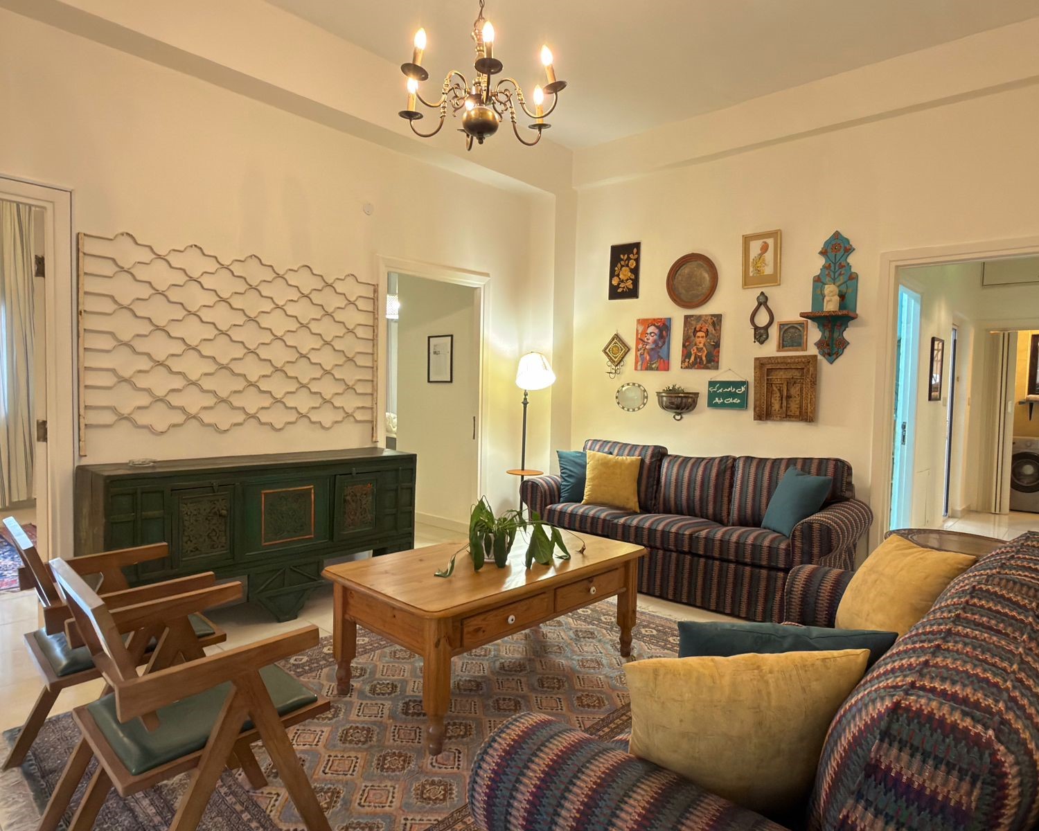 489186e7-0cbf-45f9-8042-bf00cf0b2fcf Cozy living room with striped sofas, a wooden coffee table, and a green sideboard beneath a gallery of wall art and a chandelier above.