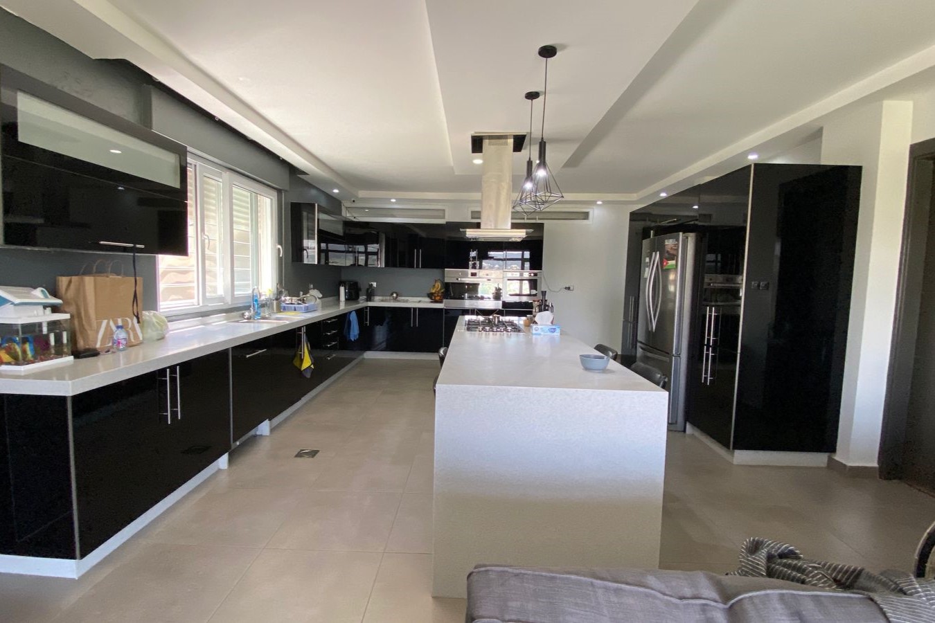 05cef65e-34a5-4cec-8e25-b1df0389c0f9 Modern kitchen with black glossy cabinets, a white island, and stainless steel appliances under pendant lights.