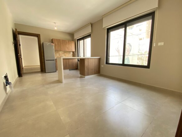 Open-concept kitchen with wooden cabinets, a fridge, and a central island under neutral tones and a large window.