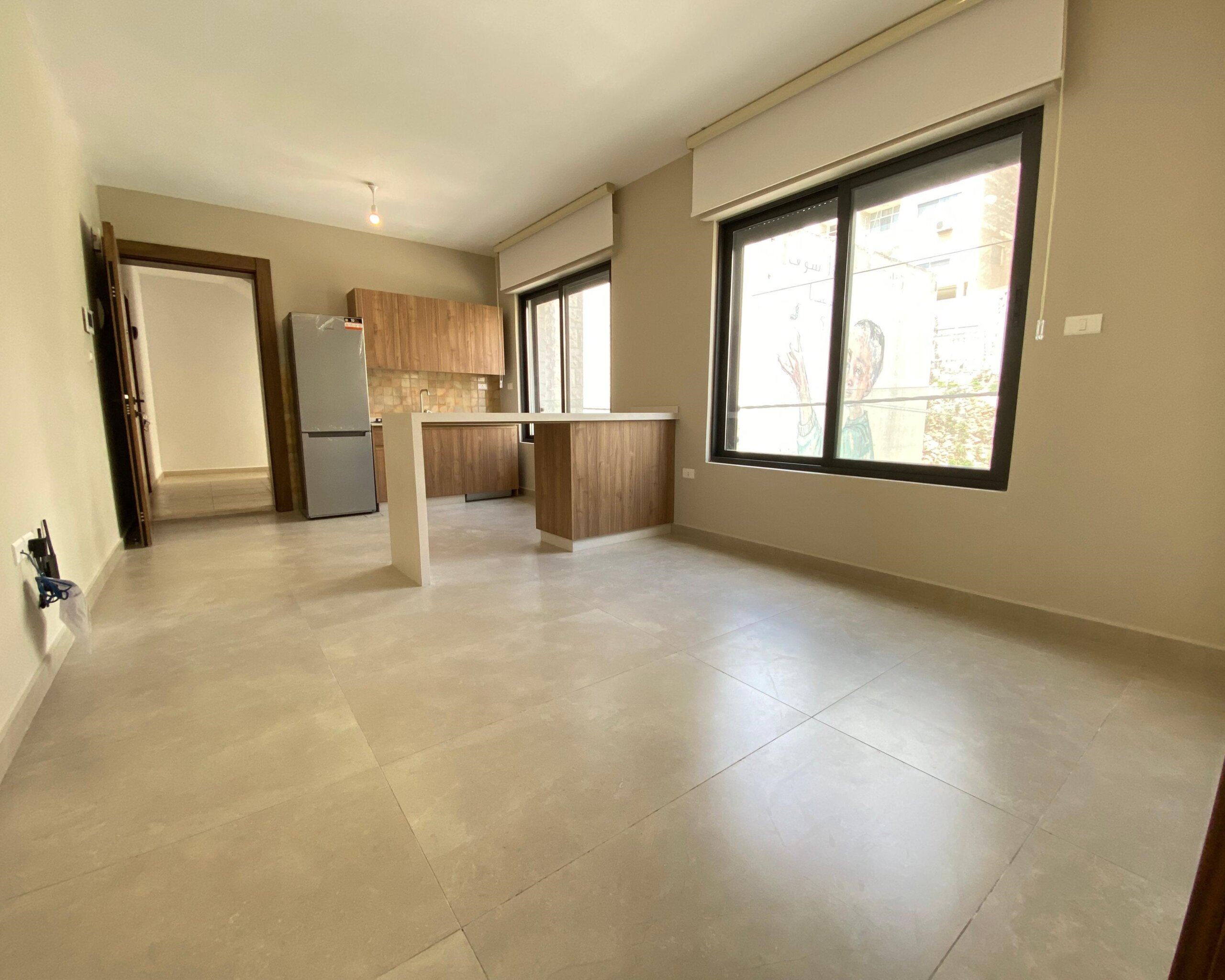 Open-concept kitchen with wooden cabinets, a fridge, and a central island under neutral tones and a large window.