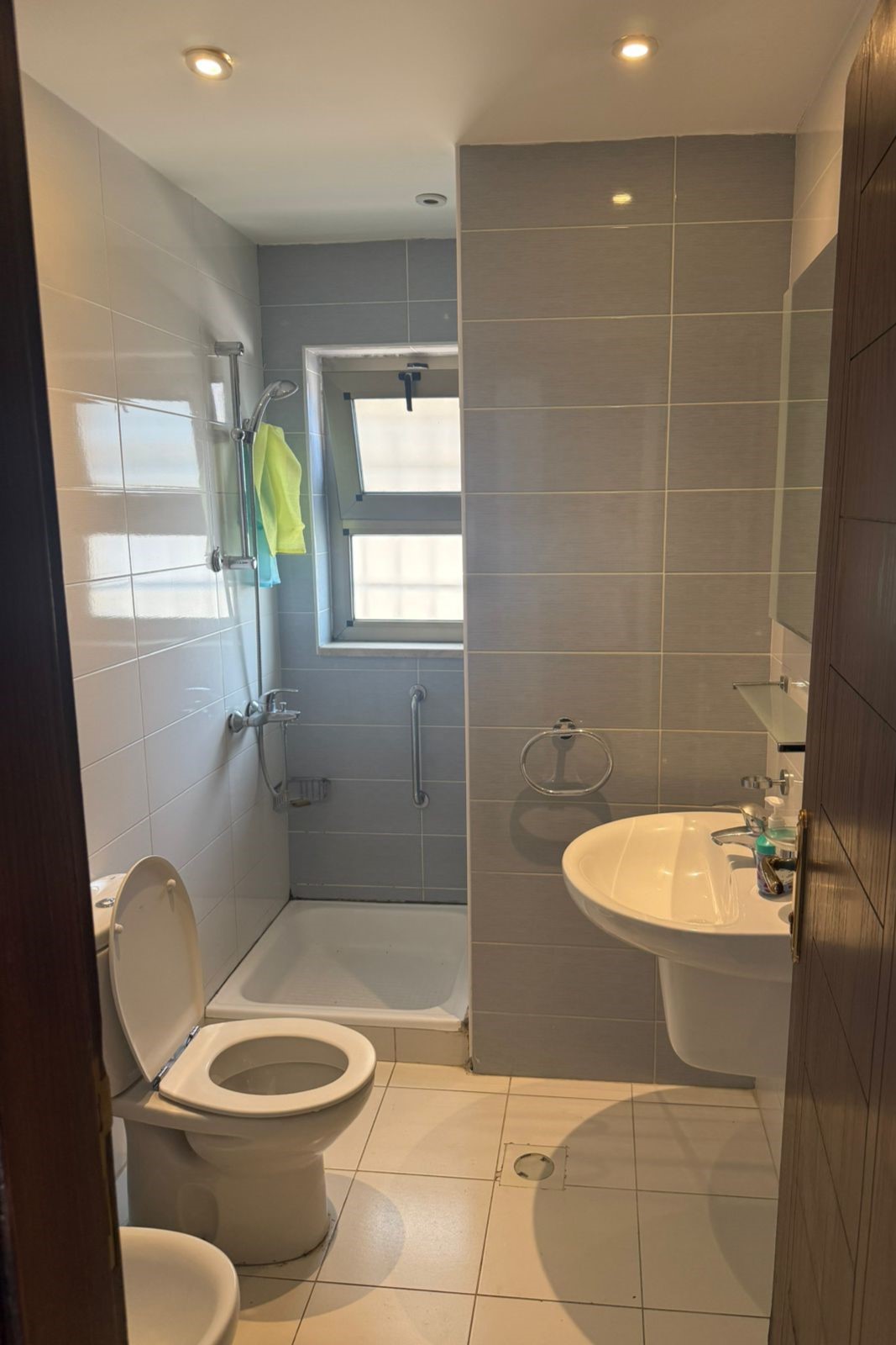 07b0d5b6-a9eb-4321-90da-439f14becbdd Small modern bathroom with shower, toilet, and wall-mounted sink; fabric towel hanging by shower and window in back corner
