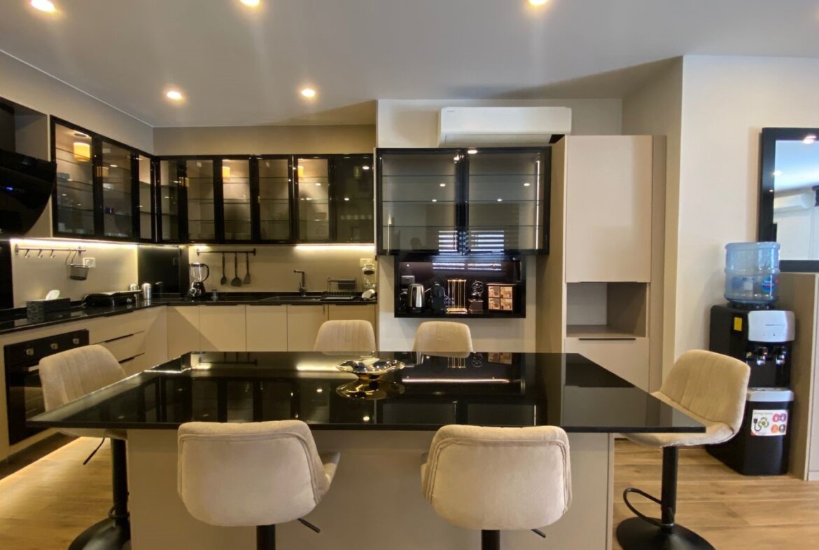 Modern kitchen with black-glass cabinets, a glossy black island, beige stools, and a water cooler in the corner.