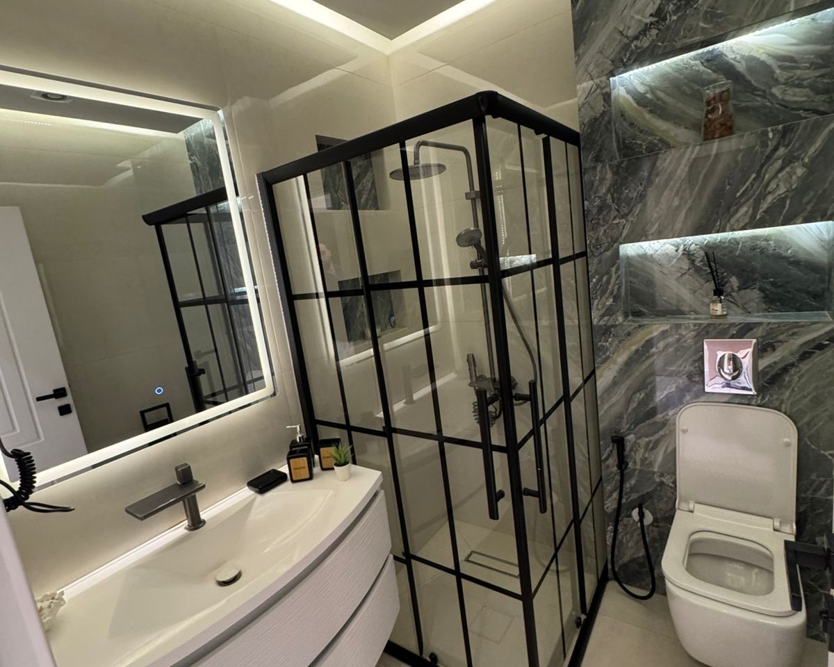 11975a76-fa62-4377-a733-ffe99ba5d0ea Modern bathroom with a glass-framed shower, white vanity, and marble walls.