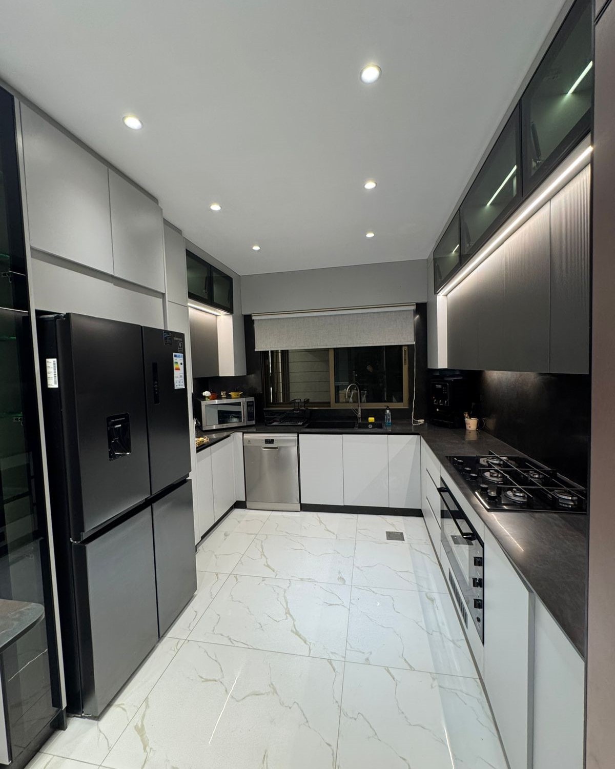 13feb5a6-018e-4f3c-85aa-1b13c39db124 Modern U-shaped kitchen with white cabinets, black countertops, and a stainless steel refrigerator and appliances.