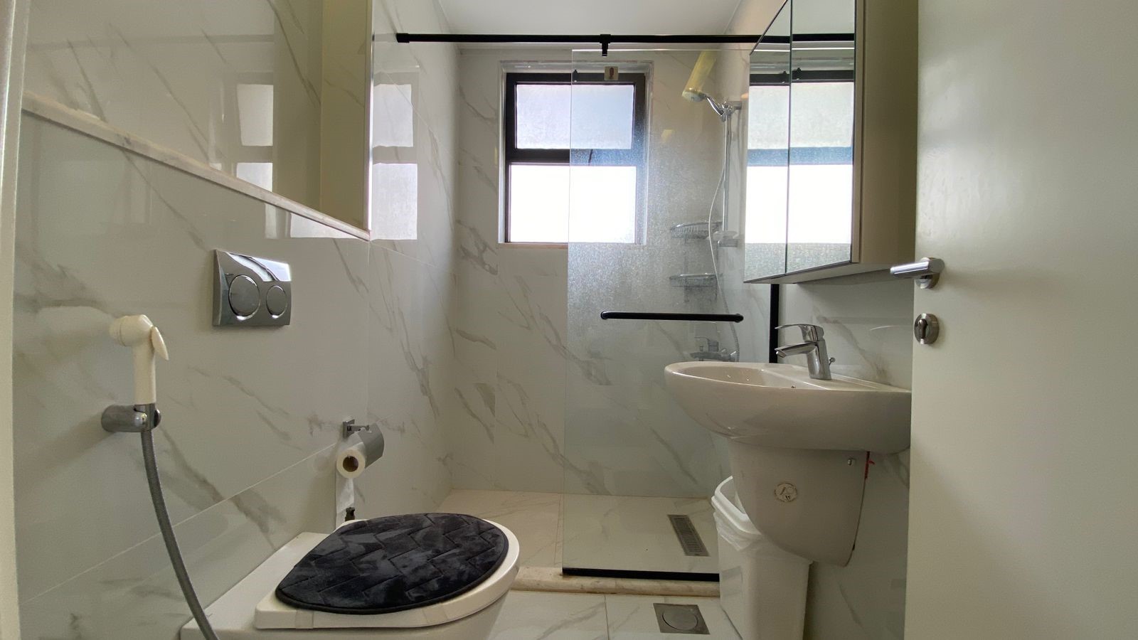 19dec9d0-b8c6-4e3d-b76c-f90aa54d661e Small modern bathroom with a glass-enclosed shower, wall-mounted flush toilet, and pedestal sink.