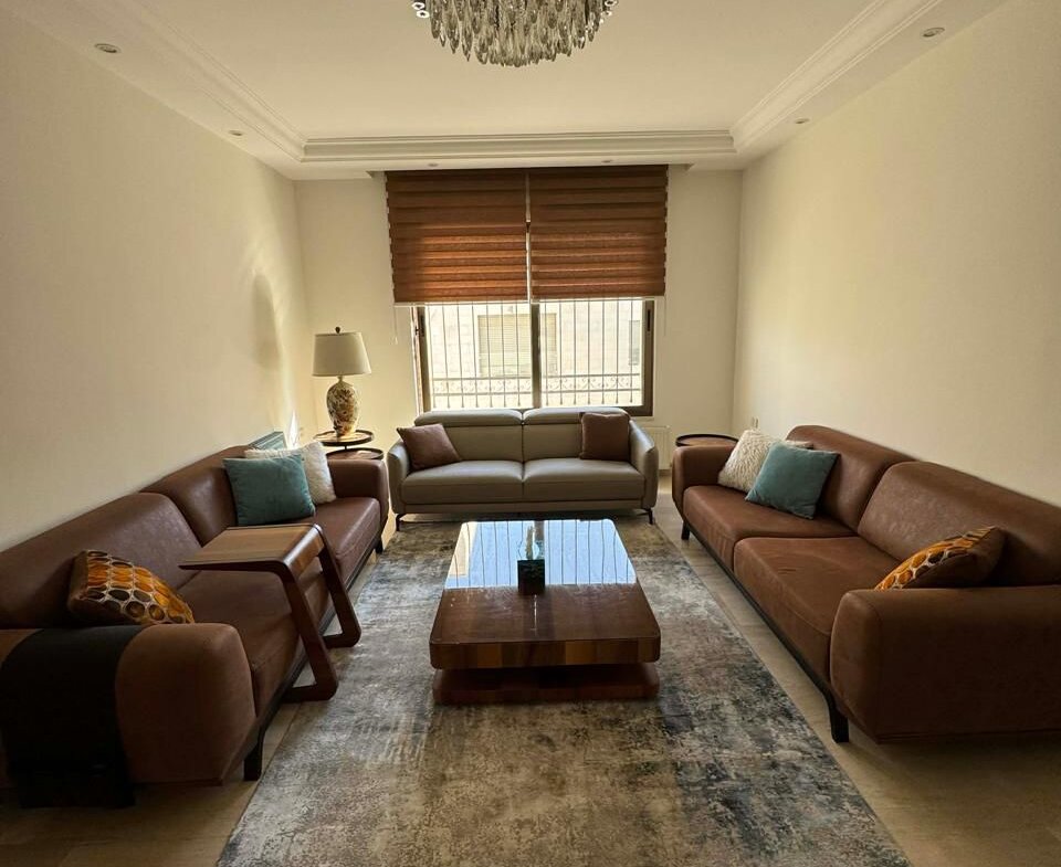 Cozy living room with brown leather sofas facing a gray sofa, a wooden coffee table, and a crystal chandelier overhead.