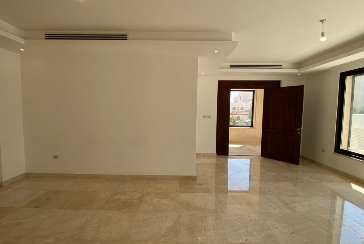 Empty modern living room with polished marble floor, white walls, large windows, and an open wooden door to a balcony/terrace.