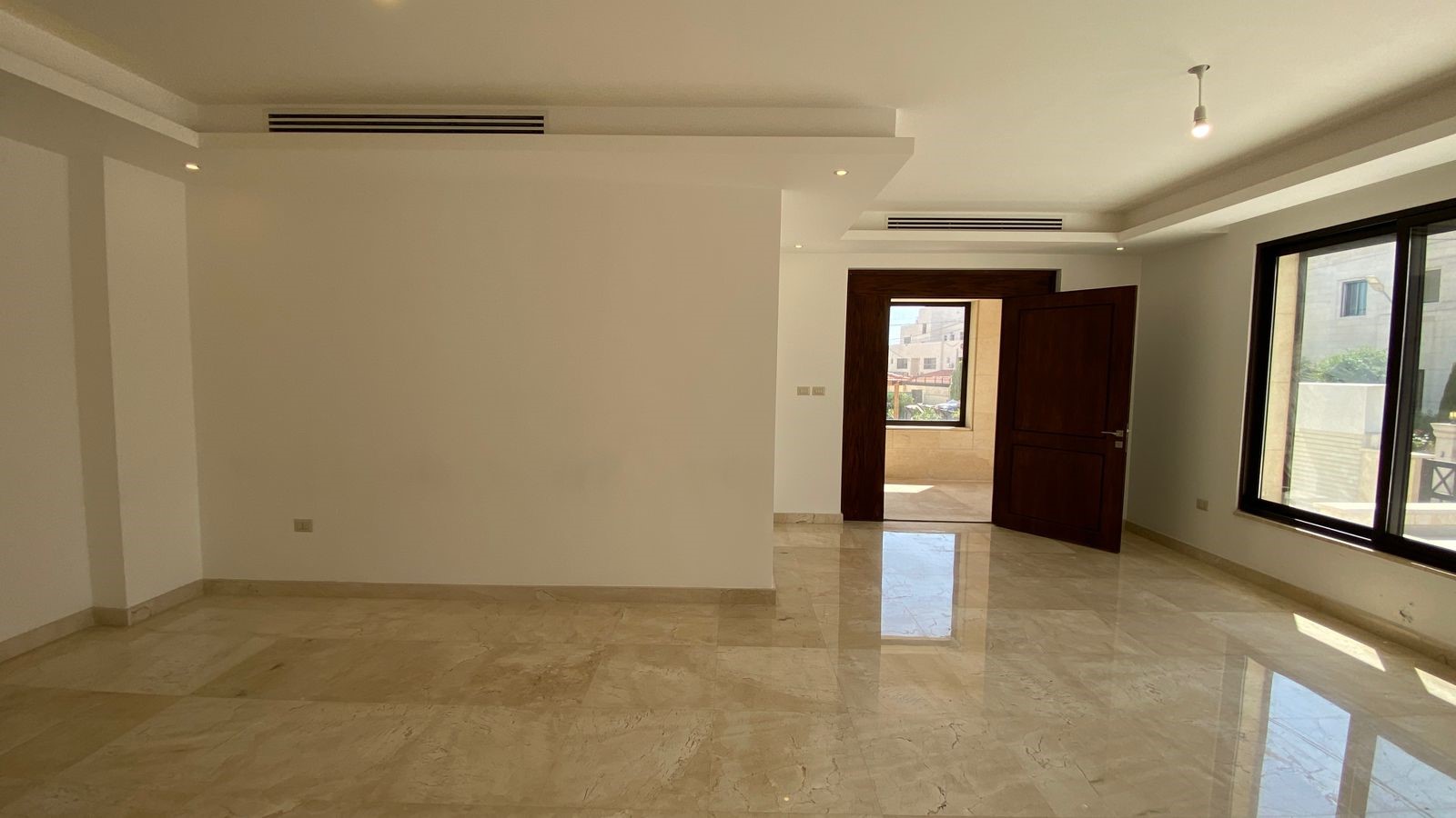 259ce45b-f6b6-4b8b-be58-10ff3f68cb6c Empty modern living room with polished marble floor, white walls, large windows, and an open wooden door to a balcony/terrace.