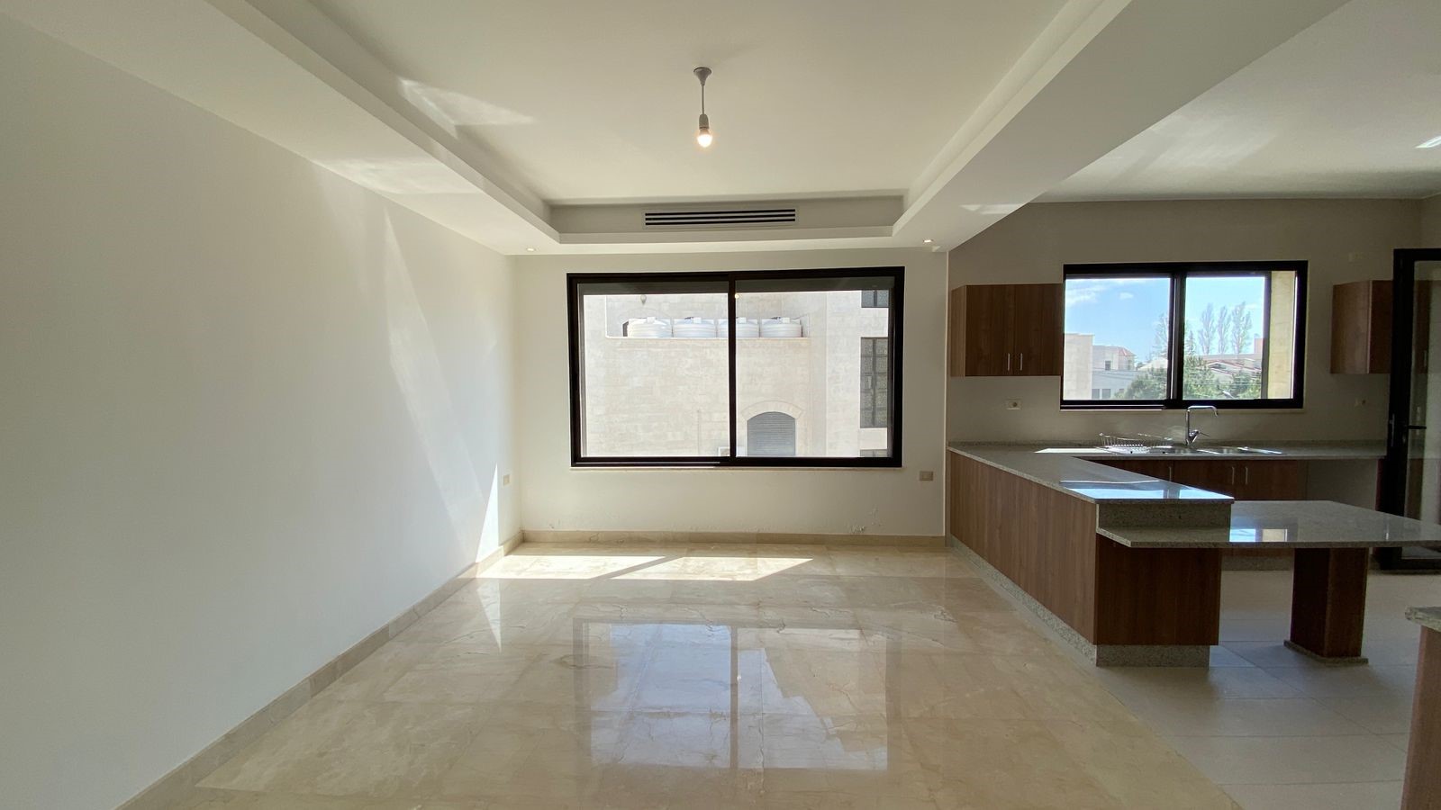 291a8f03-1e92-4f6b-894c-ec16eb1195ad Bright open-plan kitchen and living area with marble floors, large window, and wooden cabinets.