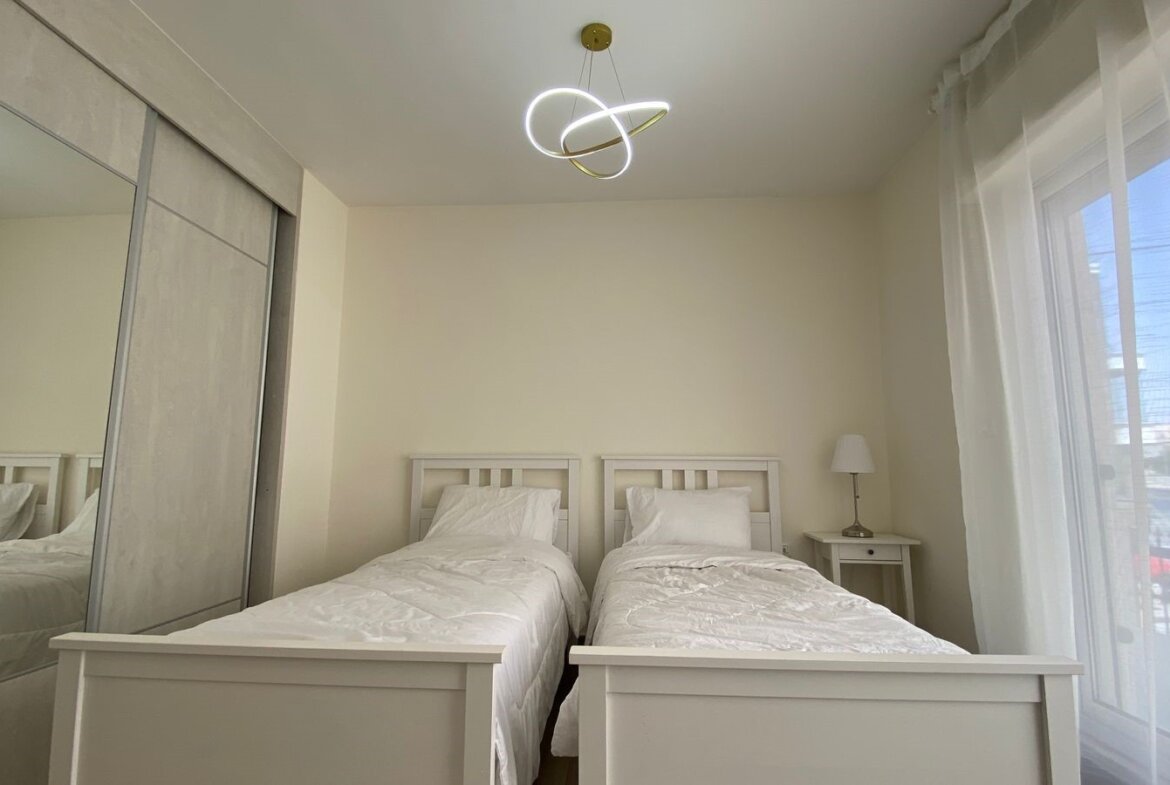 Twin bedroom with two white wooden beds, white bedding, and a nightstand with lamp between them.