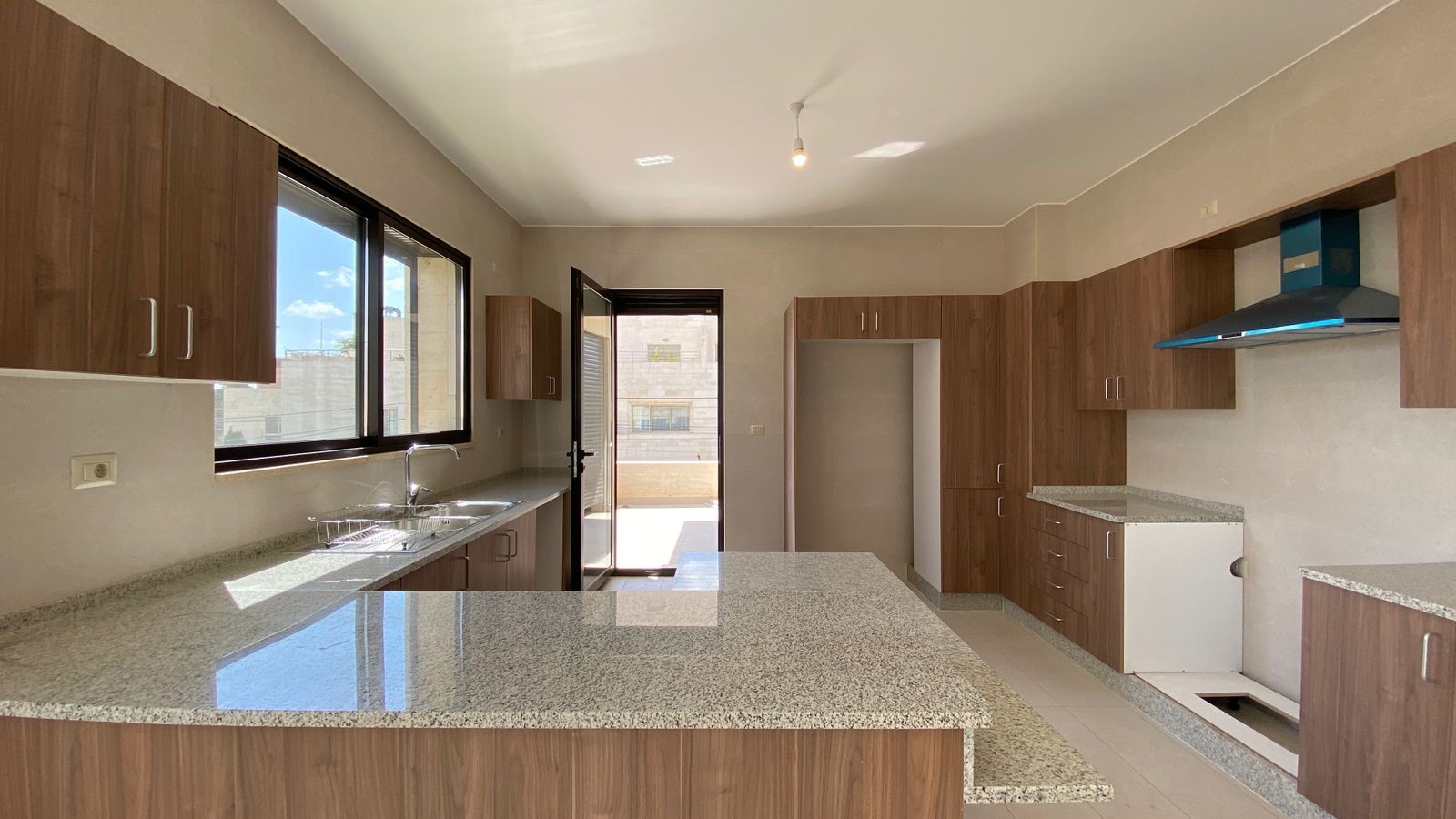 2e9979d2-f9c0-40b1-ad2a-d9d5de3b8593 Bright kitchen with wood cabinets, granite countertops, and a sink by a large window outside view of buildings/skyfalling sunlight.