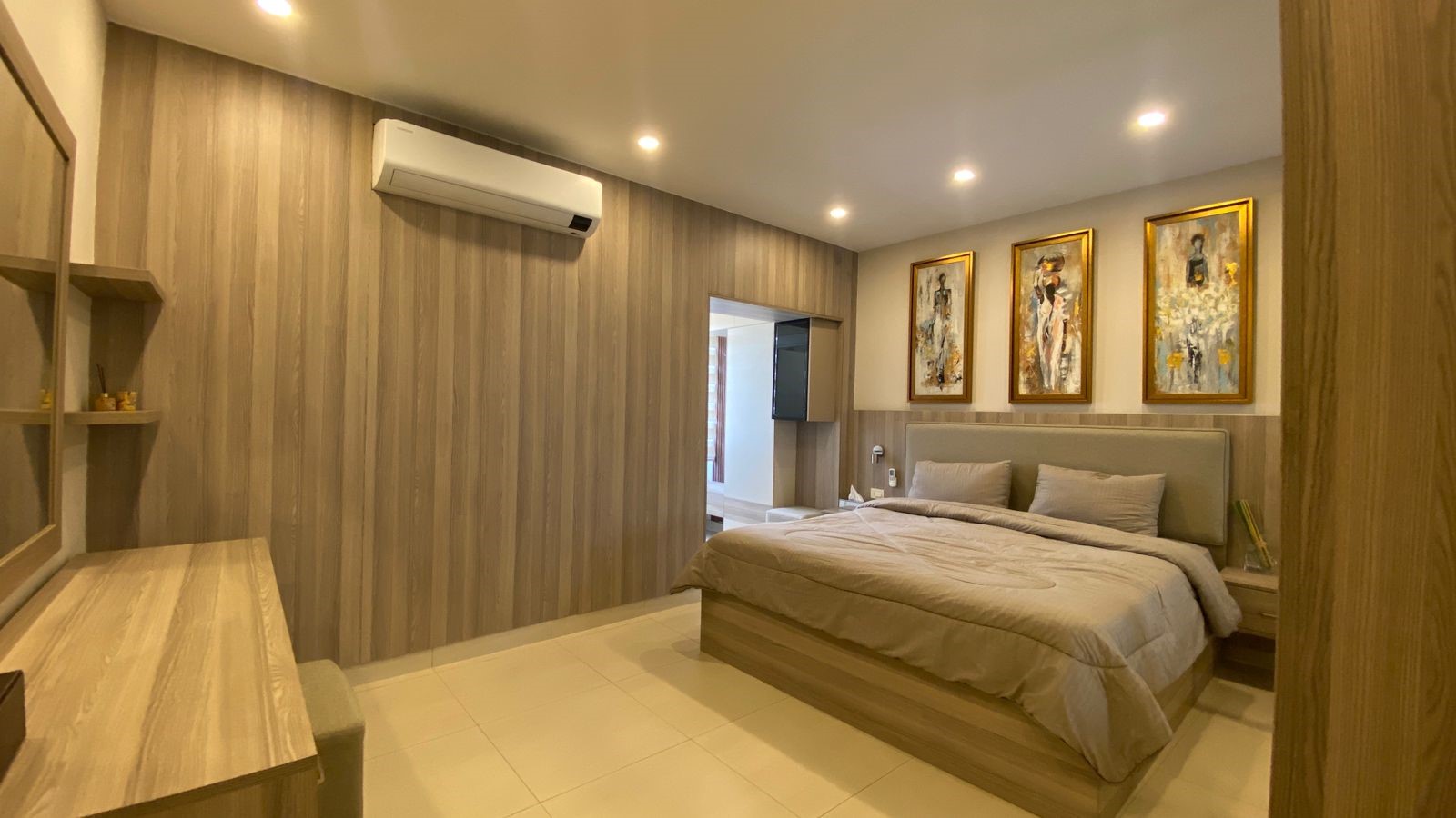 31cfe685-13b7-475b-a5f0-e127f805c88d Hotel bedroom with beige bedding, striped wooden wall, ceiling lights, and three framed paintings above the headboard.