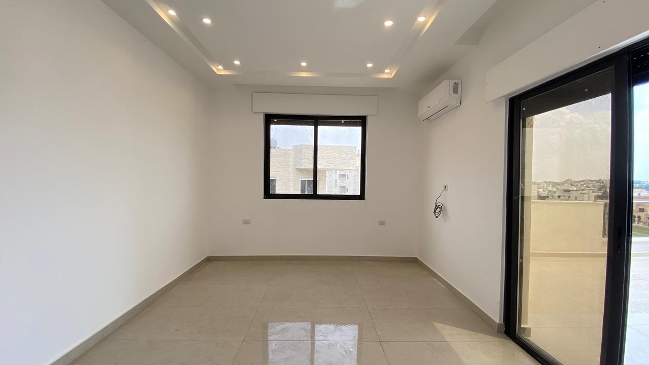 379a2b69-06ed-415b-9041-45f1c9c7ea73 Empty, unfurnished living space with white walls, glossy tile floor, and recessed ceiling lights; window and sliding balcony door visible on opposite wall.