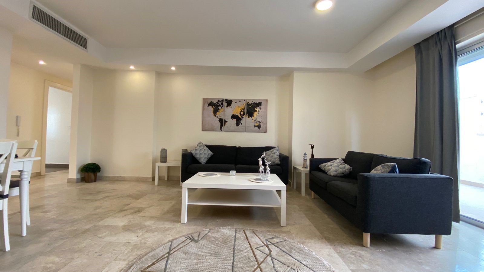 37a451dd-6059-4a0a-af24-81b1a4c431ea Modern living room with two dark gray sofas, white coffee table, world map wall art, and light gray curtains by a large window.