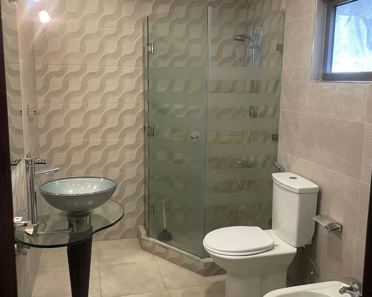 3af187df-5a7d-4601-8f87-0b6b1995d46b Modern bathroom with wavy-textured tiles, a glass vessel sink, a glass shower enclosure, and a white toilet.