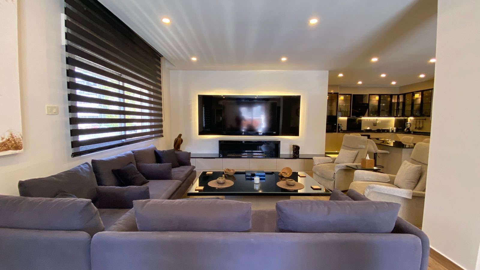 3e90ca3f-c863-4a9d-a2b0-ec4afb30eb1e Modern living room with a large gray sectional facing a wall-mounted TV framed by backlit paneling.