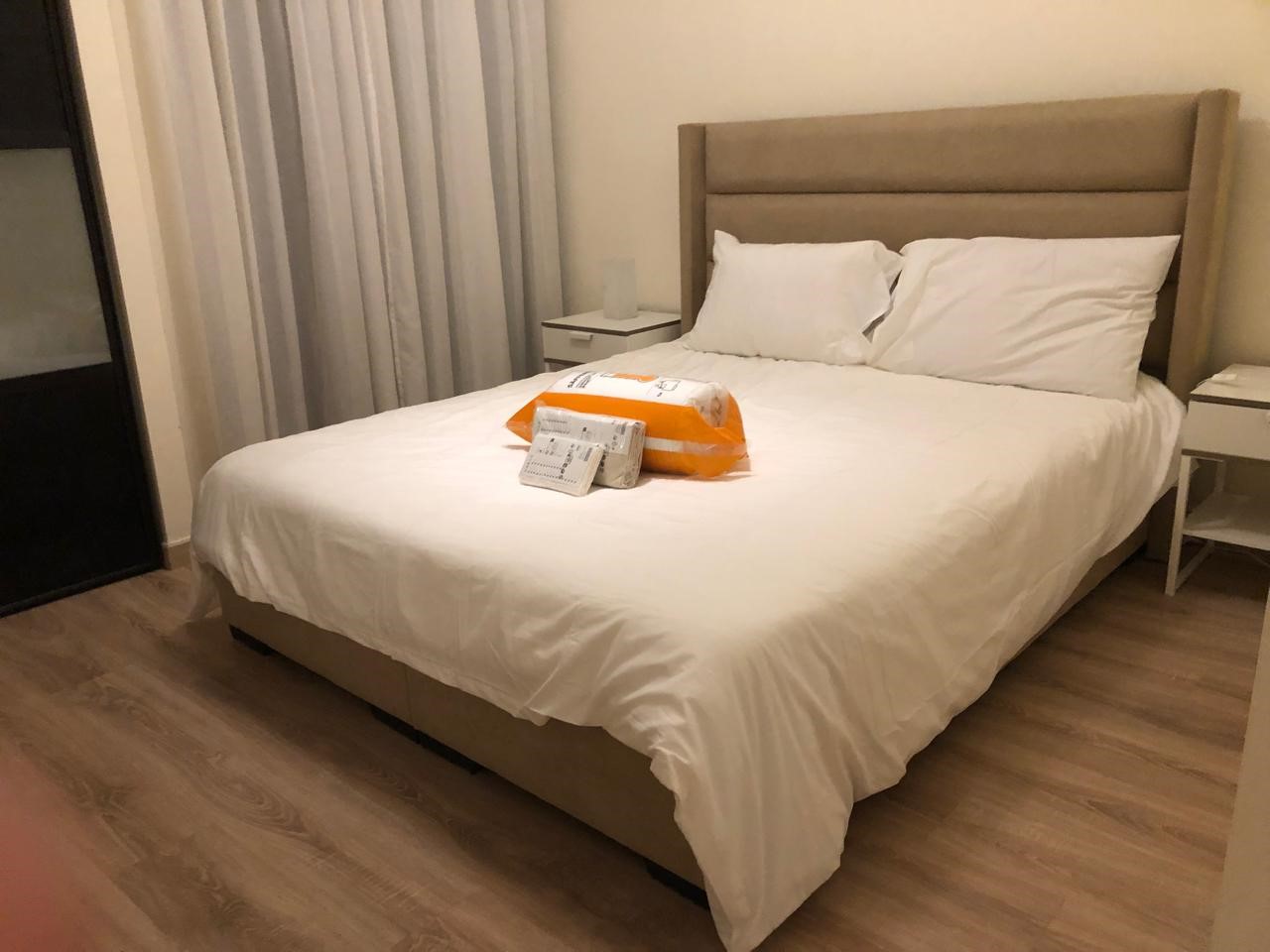 3fc30db0-9518-45f8-9bcb-9f71e9d62770 Hotel-style bedroom with a large bed in white linens, two pillows, and nightstands on either side; packages rest on the duvet.