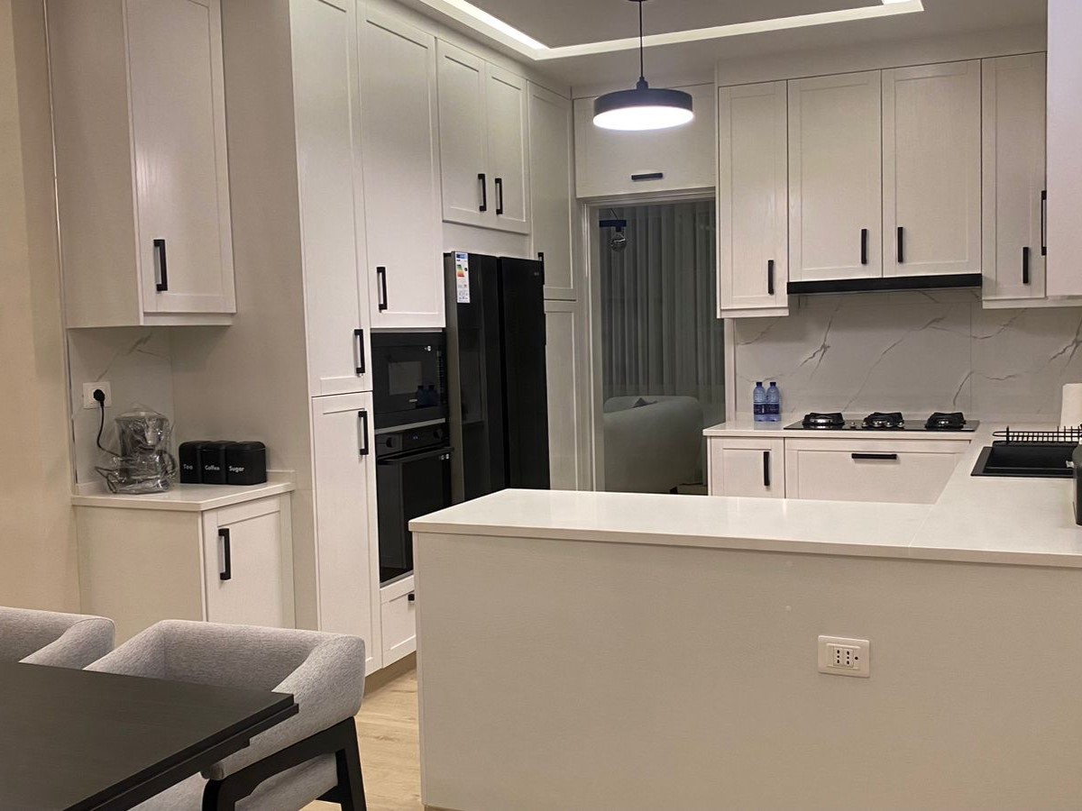 428c57b3-337a-41a7-b6d4-19cd3e3a6659 Modern white kitchen with an island, black appliances, and marble backsplash; pendant light overhead and light wood floor
