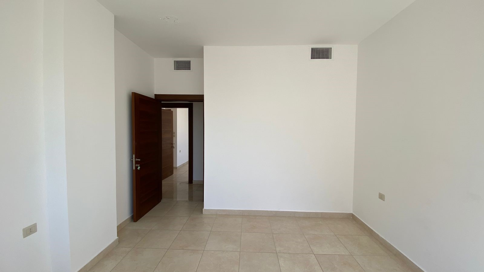 431928fb-36fd-4c65-8813-55e92d1f769a Empty white room with tiled beige floor and an open wooden door leading to a hallway.