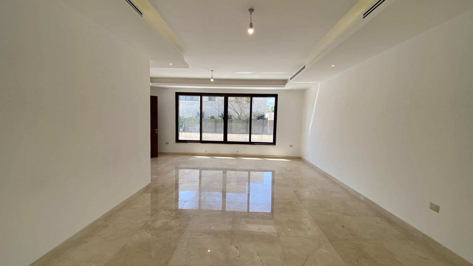 43ea5ae4-a489-4583-93de-4ad5f9d4fff8 Spacious empty living room with marble floor, white walls, and a large three-panel window letting in natural light.