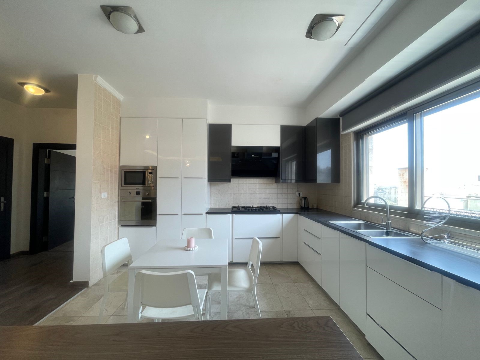 453007e5-0804-432f-a7db-e840018032b3 Bright modern kitchen with white cabinets, built-in oven, gas cooktop, and a large window over the sink area.