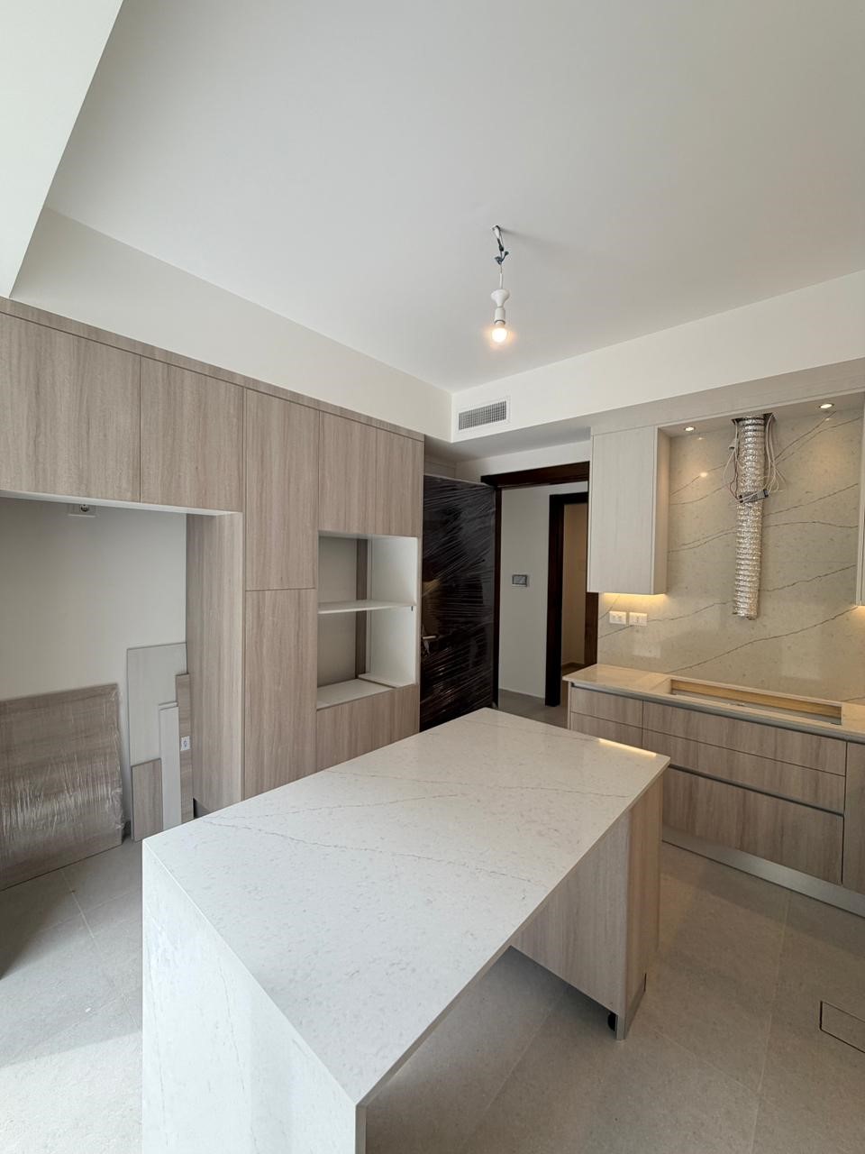 4586d507-3706-461e-bbf9-aa2e1c49cb90 Modern kitchen with light wood cabinets, a white quartz island, and built-in shelves against a marble backsplash.