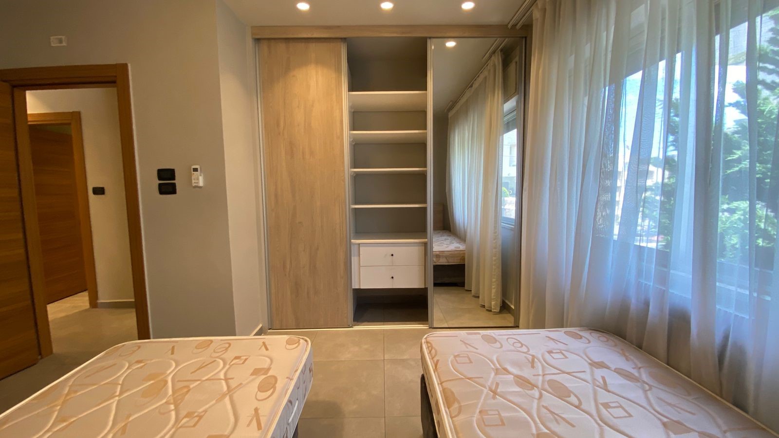 4ae44b32-eec9-4932-8b45-917197264d36 Bedroom with two single beds and a built-in wardrobe with open shelves and white drawers.