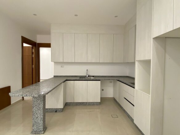 Modern white kitchen with granite counters and an island, L-shaped cabinets, and a sink in the back wall.
