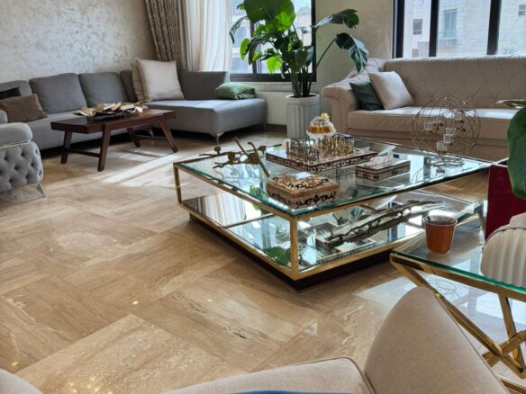 Bright living room with beige marble flooring, gray and cream sofas, and a glass coffee table with decorative items.