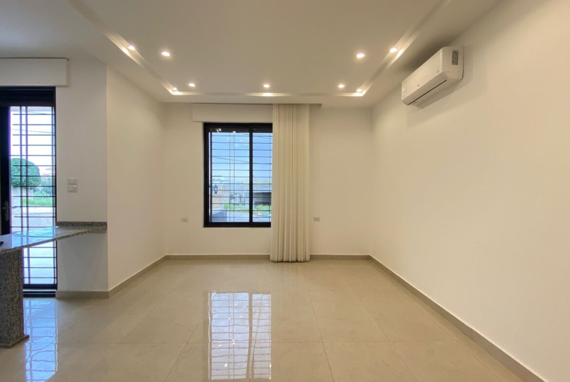 Empty living room with glossy tile floor, white walls, recessed ceiling lights, a large window with a white curtain, and a wall-mounted AC.