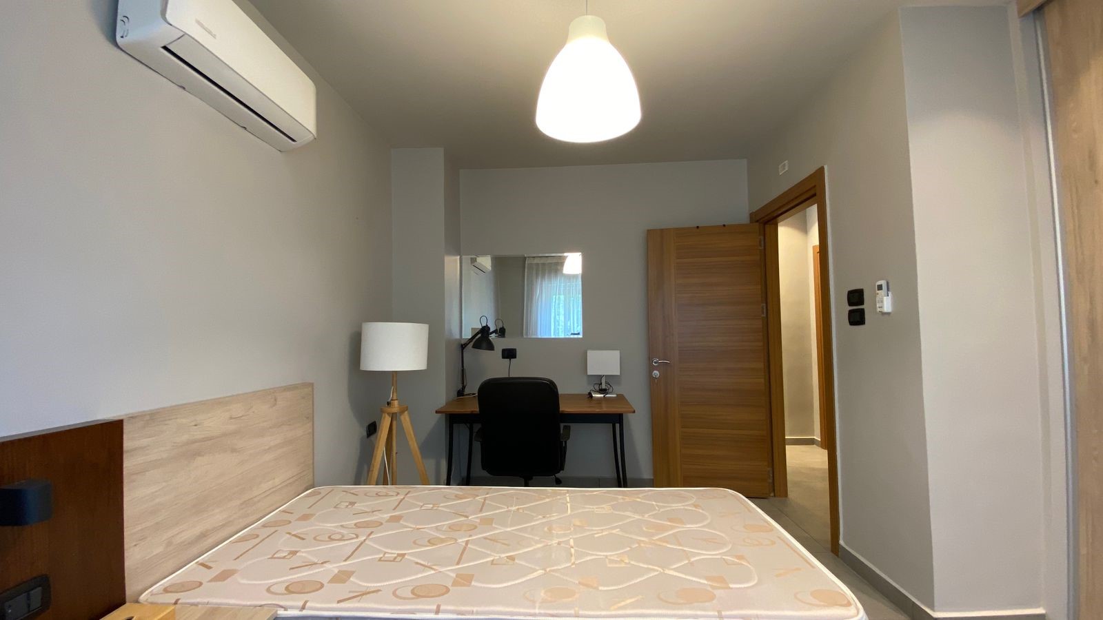 53f230b3-e2b9-4597-aab1-cb035c39e7eb Modern bedroom with a wooden headboard, a desk and chair, a floor lamp, and a ceiling pendant light.