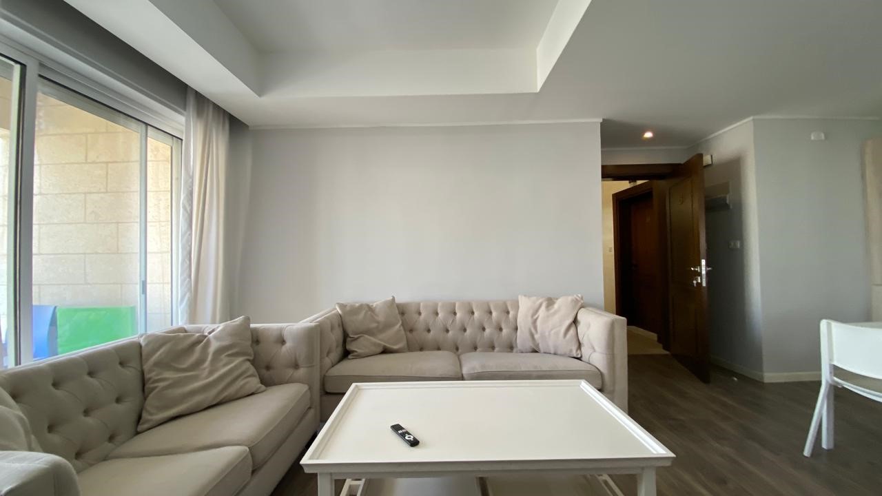 540936a5-a125-4f92-a9ec-d5907fa20050 Living room with a pale-taupe tufted sectional, cream cushions, white coffee table, and a remote on it, near a large sliding glass door.