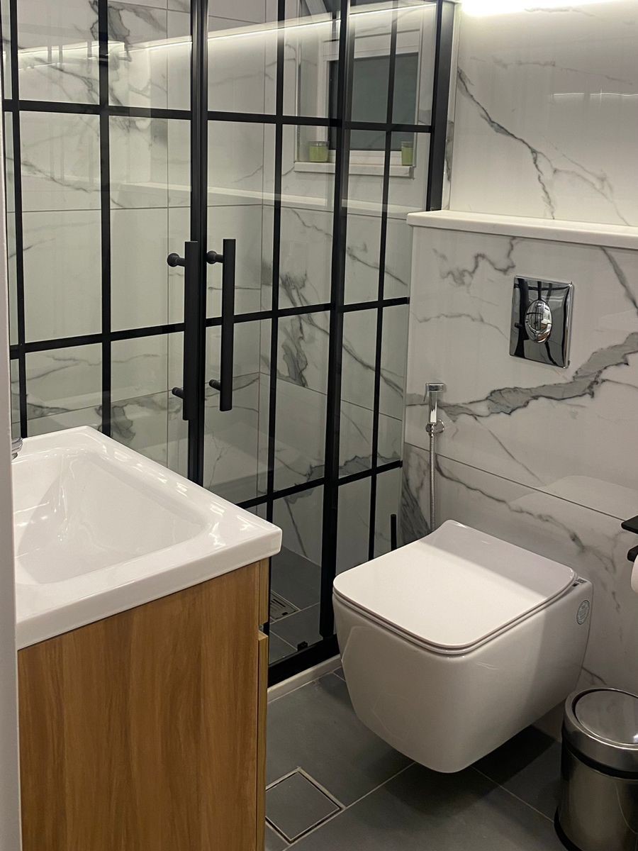 547803c0-5009-4c93-973f-362afdef86d7 Modern bathroom featuring a black-framed glass shower, marble walls, a wall-hung toilet, and a wooden vanity)