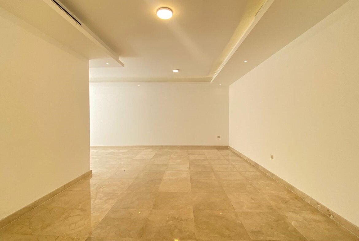 Long empty rectangular room with beige marble tile floor and white walls, lit by recessed ceiling lights
